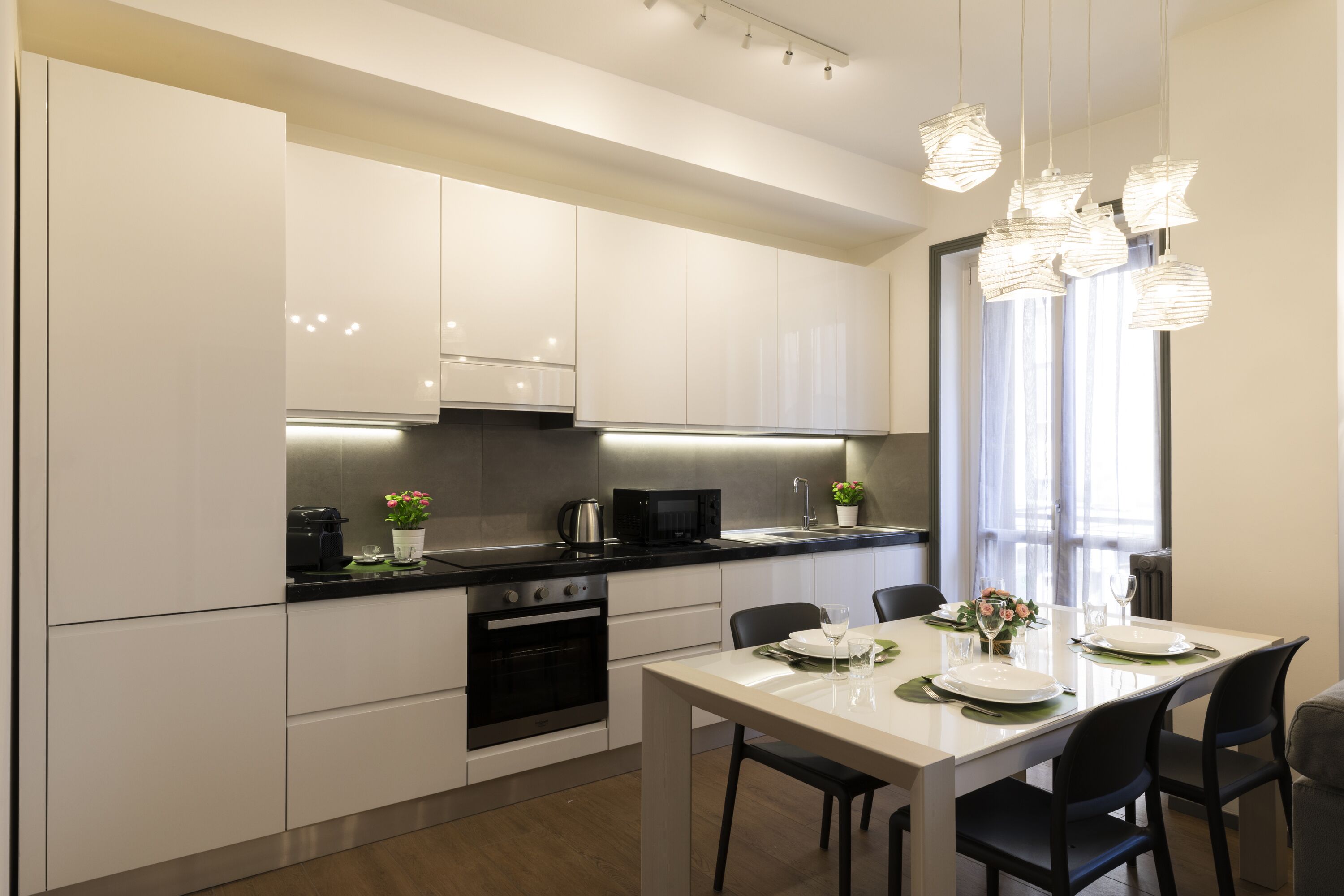 A modern kitchen with white cabinets, a black stove, and a dining area with a white table and black chairs.