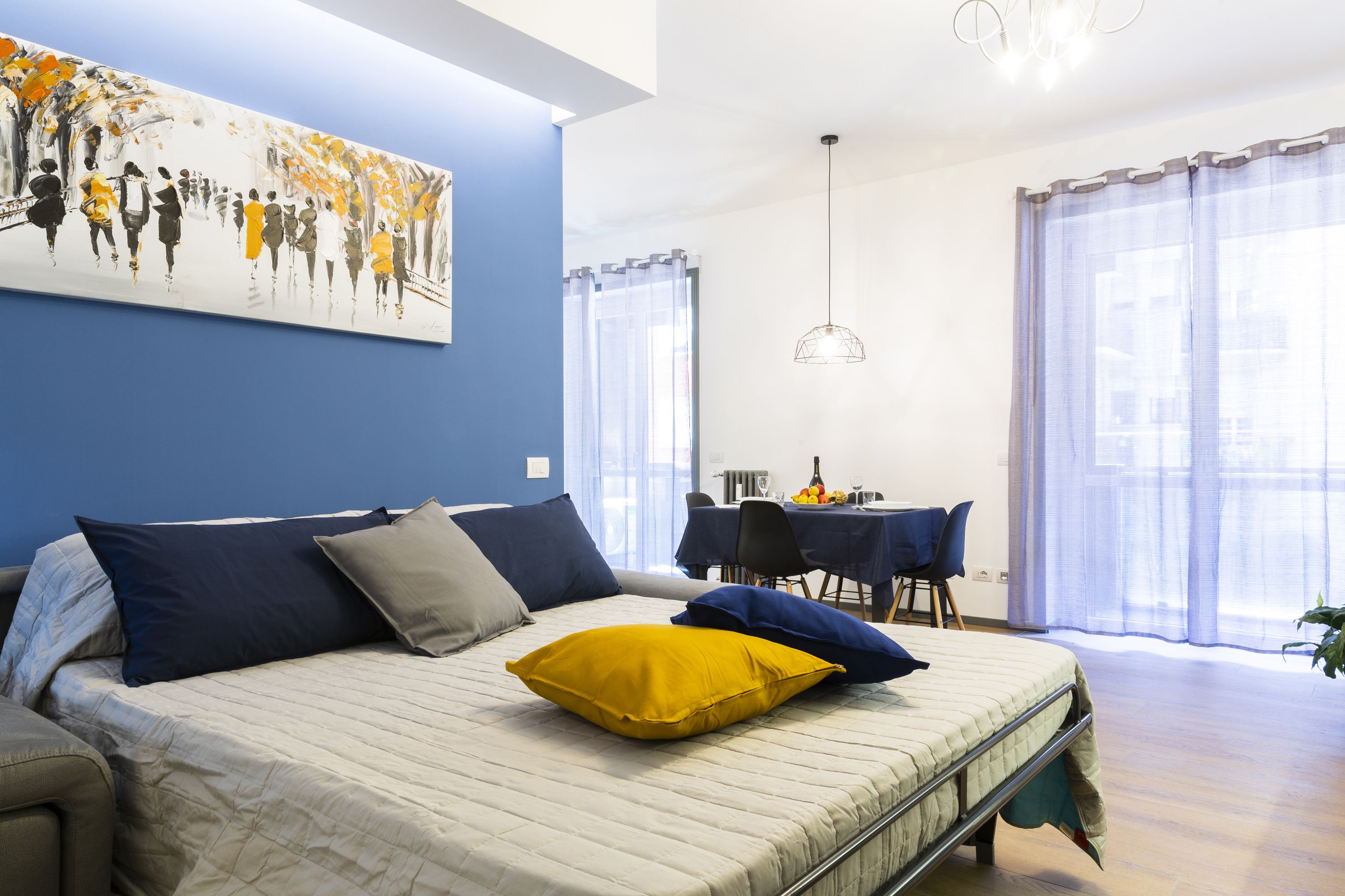 Un dormitorio moderno con cama, almohadas, un cuadro, una zona de comedor y una ventana.