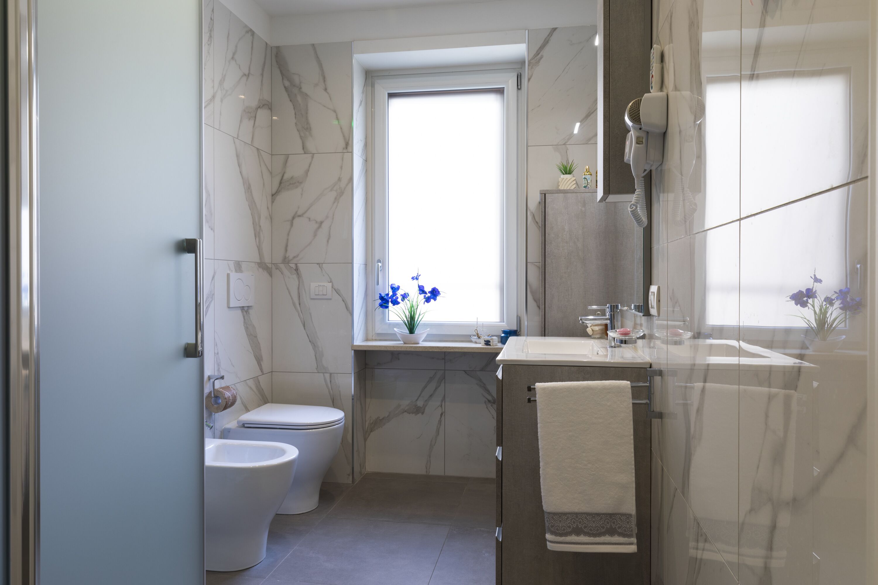 A bathroom with a toilet, bidet, sink, and a towel hanging on the wall.