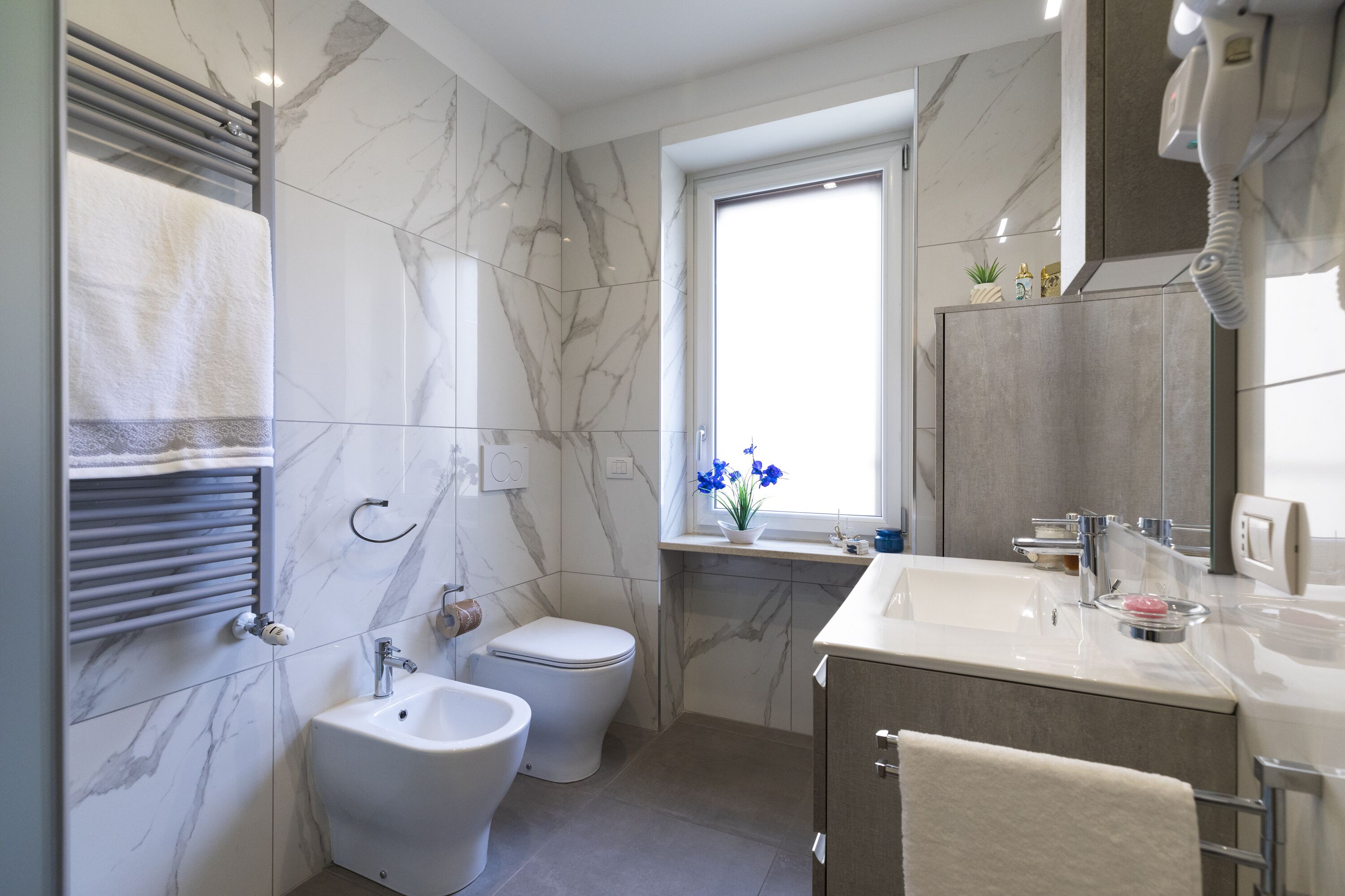 A modern bathroom with a bidet, toilet, vanity, and a window with blue flowers.