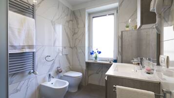 Un baño moderno con bidé, inodoro, tocador y una ventana con flores azules.