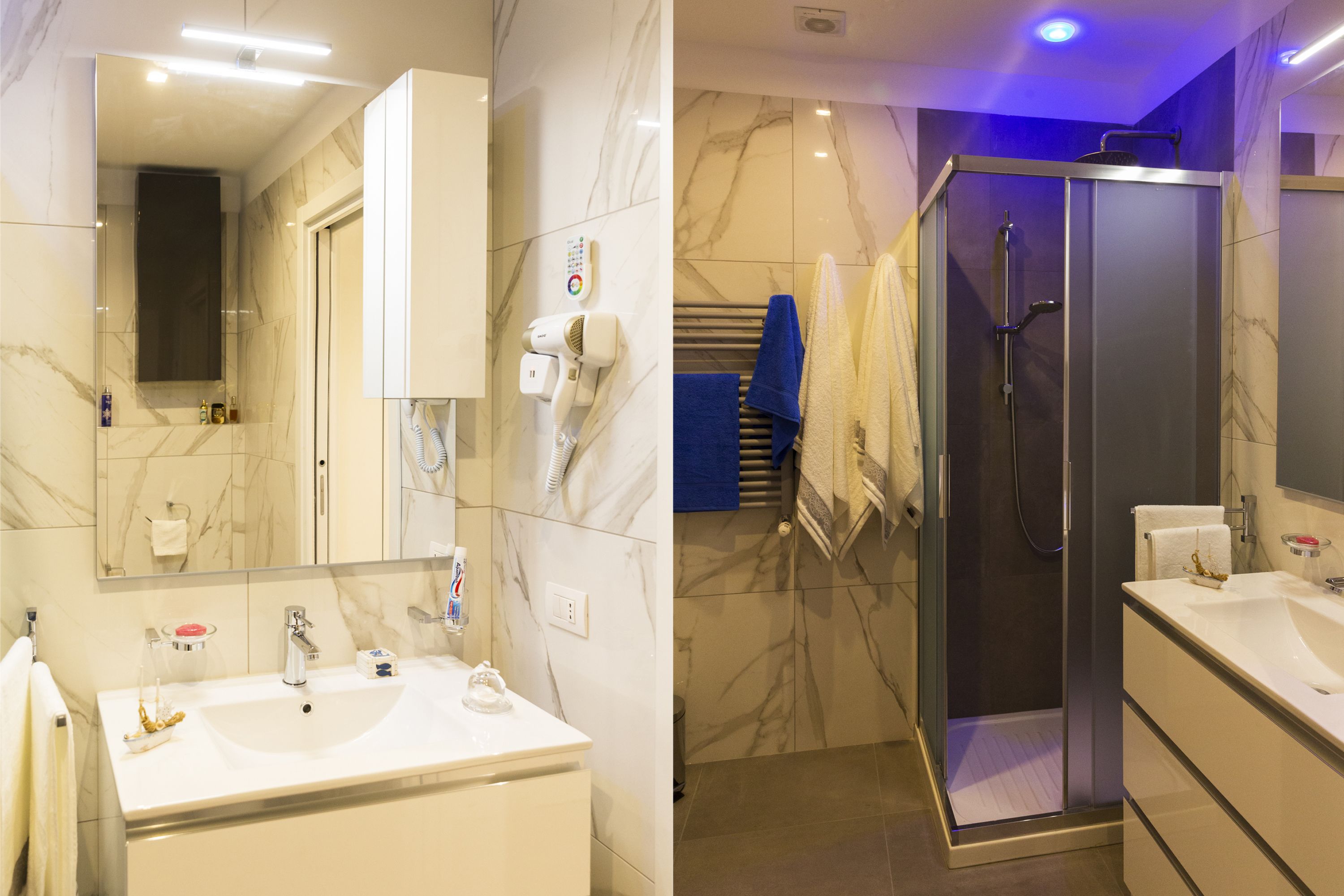 Un bagno moderno con un ampio specchio, piastrelle in marmo bianco, un lavandino bianco e una cabina doccia in vetro.