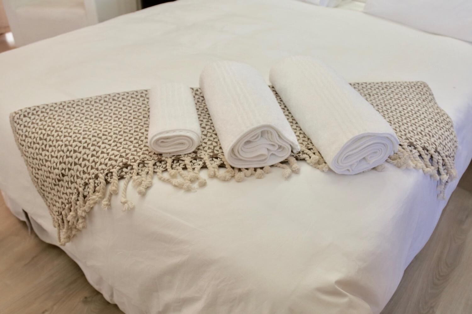 Una cama bien hecha con sábana blanca y tres toallas enrolladas.