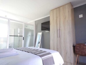 Een slaapkamer met een bed, een kledingkast, een televisie en een stoel.