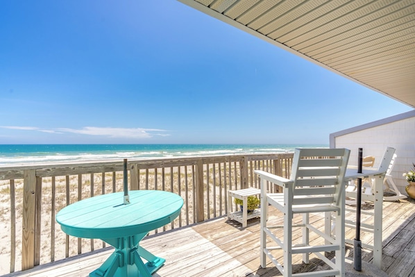 A wooden deck with a turquoise table and white chairs overlooking a beach. - Ocean Potion - Oceanfront Queen's Grant Condo with Amazing Views! (Topsail Beach)