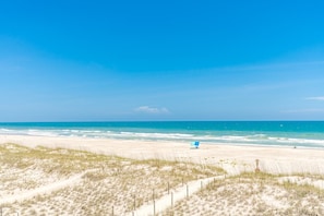 A beach with a clear sky, sandy dunes, and a blue umbrella.
