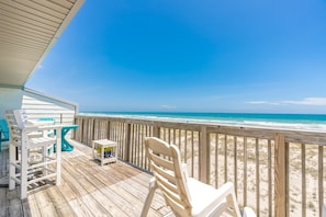 A wooden deck with a view of the beach, a white chair, and a table.