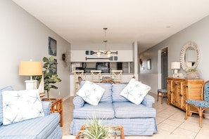 A living room with a sofa, chairs, a dining table, and a kitchen area.