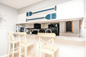 A kitchen with a white countertop, two wooden bar stools, a black refrigerator, and a black stove.