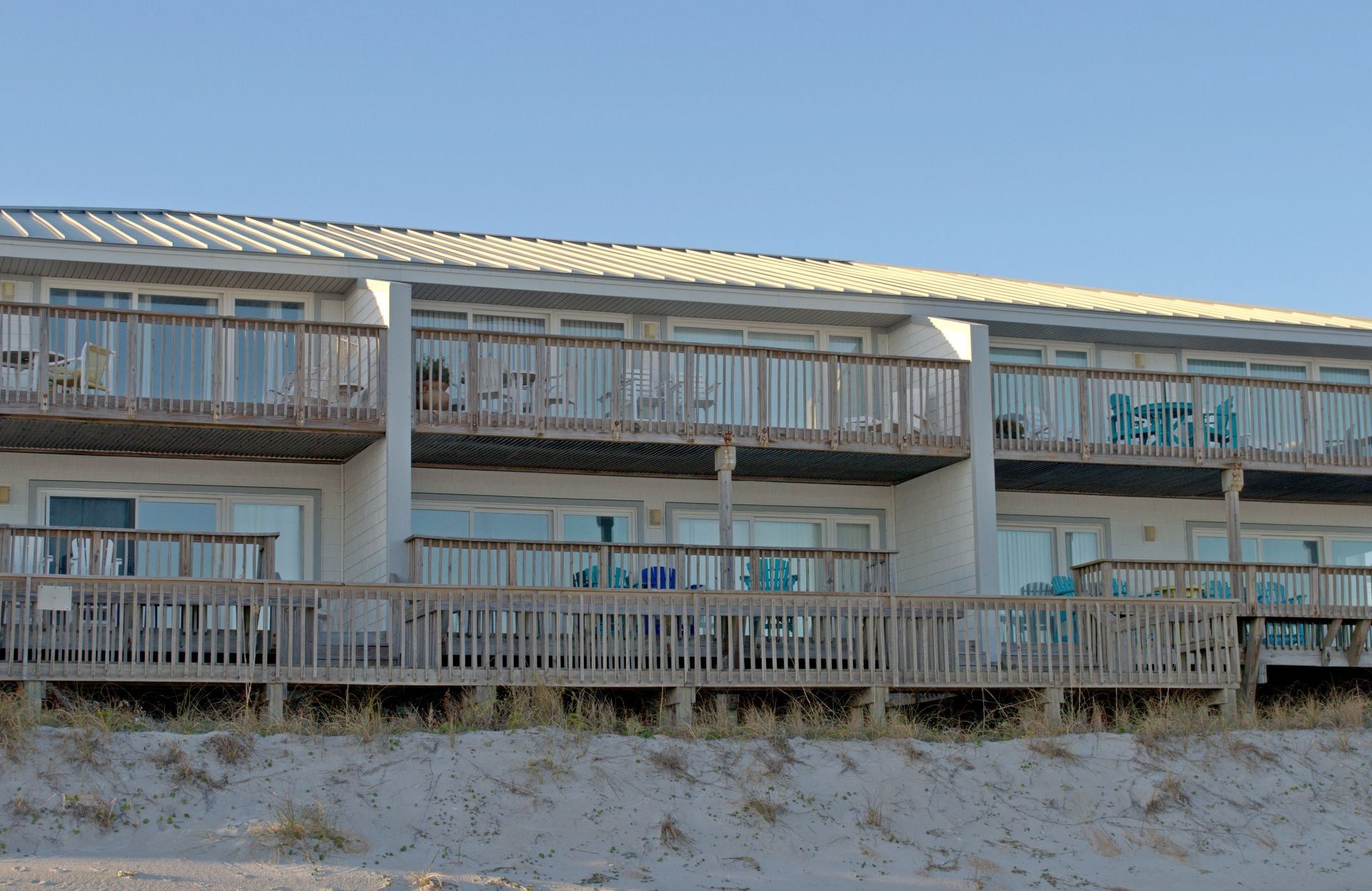 Un hôtel en bord de mer, avec plusieurs étages, des balcons, une plage de sable devant et un ciel dégagé.
