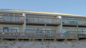 Un hôtel en bord de mer, avec plusieurs étages, des balcons, une plage de sable devant et un ciel dégagé.
