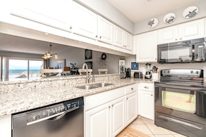 A modern kitchen with white cabinetry, granite countertops, a built-in dishwasher, a stainless steel oven, and a microwave. - Ocean Potion - Oceanfront Queen's Grant Condo with Amazing Views! (Topsail Beach)