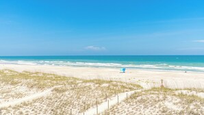 A beach with a clear sky, sandy dunes, and a blue chair. - Ocean Potion - Oceanfront Queen's Grant Condo with Amazing Views! (Topsail Beach)