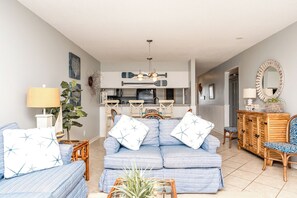 A living room with a sofa set, a dining area, and a kitchen. - Ocean Potion - Oceanfront Queen's Grant Condo with Amazing Views! (Topsail Beach)