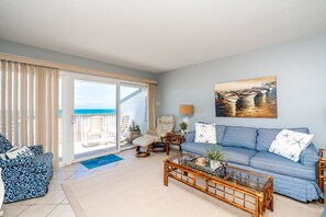 A living room with a sofa, armchairs, a coffee table, and a painting of boats.