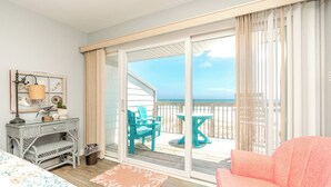 Une chambre comprenant un lit, un bureau, une chaise, une table et une vue sur la plage, accessible par une porte coulissante.