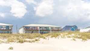 En byggnad som ligger vid stranden, med flera balkonger, en sandstrand framför och en klar himmel.