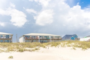 A beachfront building with multiple balconies, a sandy foreground, and a clear sky.