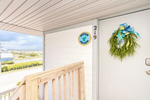 A wooden deck with a view of a coastal landscape, a door with a number sign, and a decorative wreath. - Ocean Potion - Oceanfront Queen's Grant Condo with Amazing Views! (Topsail Beach)