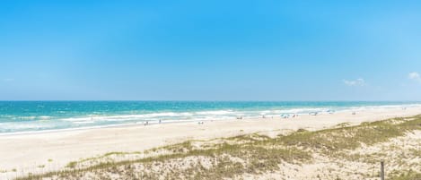 A beach with a wooden boardwalk leading to the water, sandy dunes, and a clear blue sky.