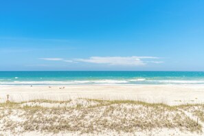 A beach with a clear sky, sandy shore, and sparse vegetation. - Ocean Potion - Oceanfront Queen's Grant Condo with Amazing Views! (Topsail Beach)