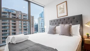 A hotel room with a large bed, grey headboard, and a view of city buildings. - City Living At Best Location In Melbourne (Melbourne)