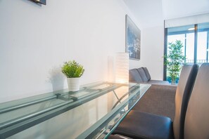 Een moderne woonkamer met een glazen salontafel, een potplant, een bank en een groot raam met uitzicht op de omgeving.