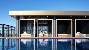 A modern hotel with a pool area, featuring a large pool, outdoor seating, and a contemporary design. - Luxury 1 Bedroom 1 Study With 1 Parking (Wentworth Point)