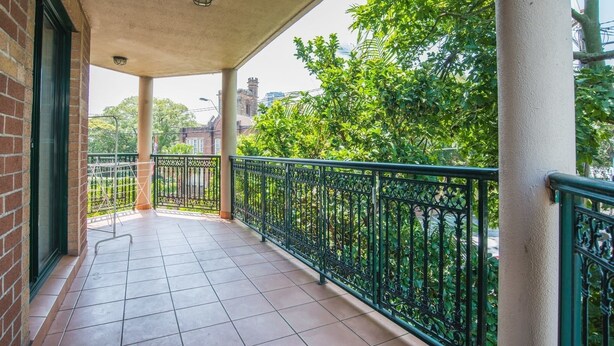 A balcony with tiled flooring, a metal railing, and a view of greenery and buildings in the background. - Spacious & Cozy Apartment In Heart Of Redfern (Redfern)