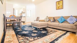 A living room with a sectional sofa, a dining table with chairs, and a patterned rug. - Spacious & Cozy Apartment In Heart Of Redfern (Redfern)