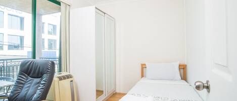 A small, clean room with a bed, a chair, and a heater.