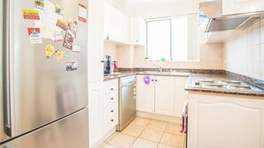 A modern kitchen with white cabinets, a stainless steel refrigerator, a granite countertop, and a window above the sink. - Spacious & Cozy Apartment In Heart Of Redfern (Redfern)