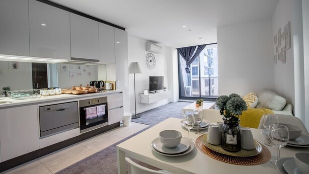A modern kitchen with white cabinets, a built-in oven, and a dining area with a table set for two. - New Renovated & Cozy Apt Closes To Southern Cross (Melbourne)