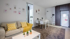 A modern living room with a beige sofa, a coffee table with potted plants, and a dining area with a white table and chairs. - New Renovated & Cozy Apt Closes To Southern Cross (Melbourne)