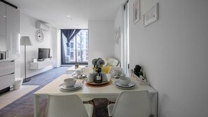 A modern dining area with a table set for four, a sofa, and a television in the background. - New Renovated & Cozy Apt Closes To Southern Cross (Melbourne)