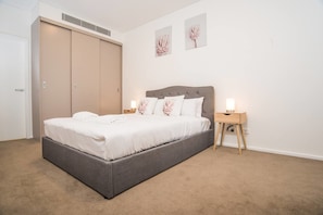 A bedroom with a bed, bedside tables, a wardrobe, and two wall-mounted artworks.