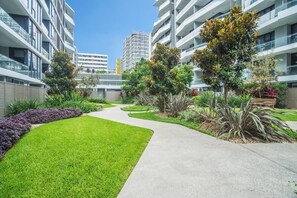 Un immeuble d’appartements moderne doté d’un chemin central, entouré d’une végétation luxuriante et d’arbres matures.