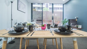 Une salle de conférence avec une table en bois, préparée pour une réunion, et équipée d’assiettes, de tasses et de couverts noirs.