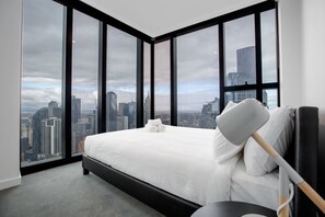Une chambre d’hôtel moderne dotée d’un grand lit, d’une table de chevet et offrant une vue sur le paysage urbain grâce à de grandes fenêtres du sol au plafond.