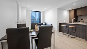 Une cuisine moderne avec des meubles de couleur sombre, un îlot central doté de tabourets et un coin repas avec une table et des chaises.