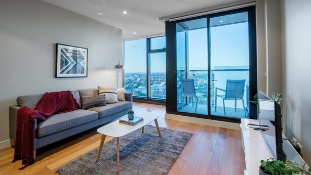 A modern living room with a grey sofa, a white coffee table, and a large window offering a city view. - Sweet Apartment At Centro Melbourne (Melbourne)