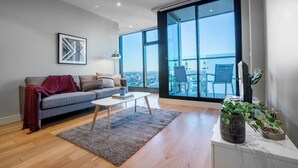 A modern living room with a grey sofa, a coffee table, and a large window offering a city view. - Sweet Apartment At Centro Melbourne (Melbourne)