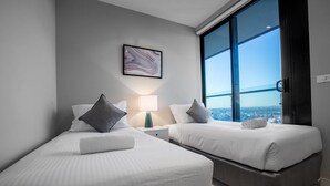 A modern hotel room with two beds, a nightstand, a lamp, and a large window offering a city view. - Sweet Apartment At Centro Melbourne (Melbourne)