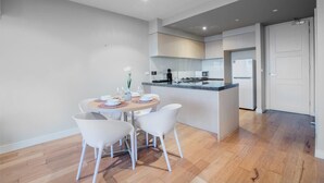 A modern kitchen with a central island, white cabinetry, and a dining area with a round table and white chairs. - Sweet Apartment At Centro Melbourne (Melbourne)