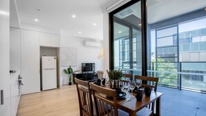 A modern kitchen with white cabinets, a black refrigerator, and a dining area with wooden chairs and a table set for four. - Stunning Bright Apartment At Hawthron/Glenferrie Station (Hawthorn)