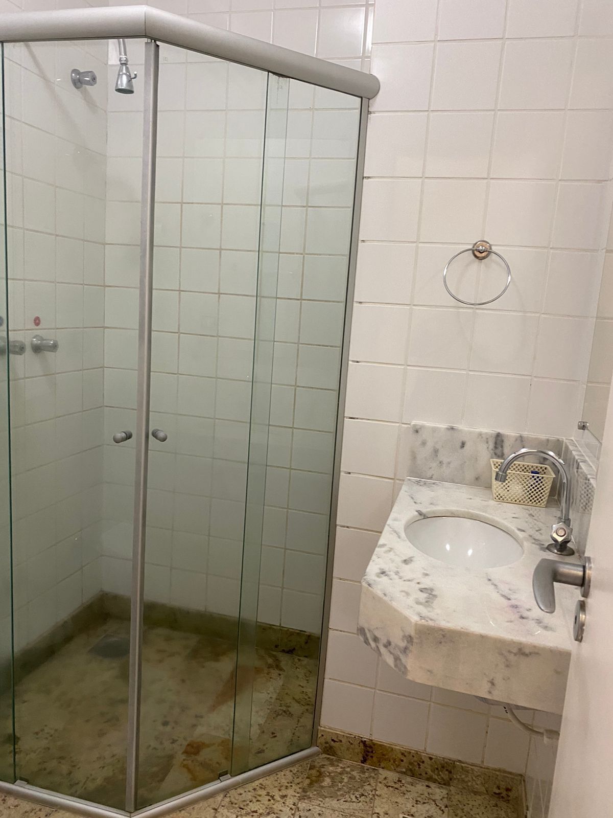 Un baño con cabina de ducha de vidrio, lavamanos de mármol y un aro para toallas en la pared.
