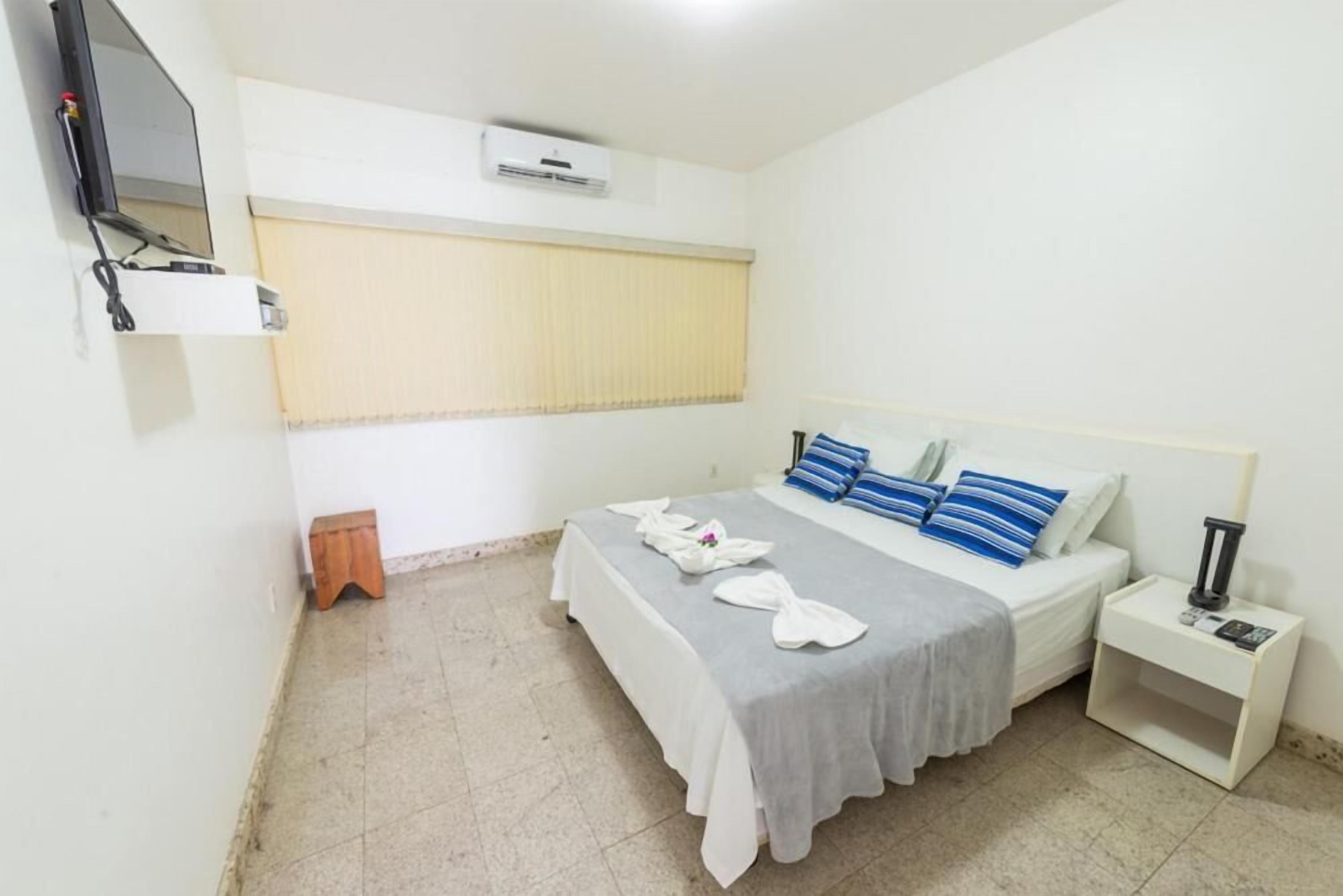 A bedroom with a bed, a nightstand, a TV, and an air conditioning unit.