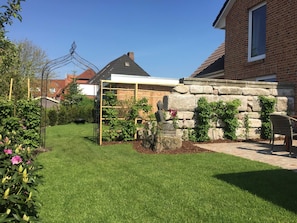 A backyard with a garden, a stone wall, and a wooden pergola.