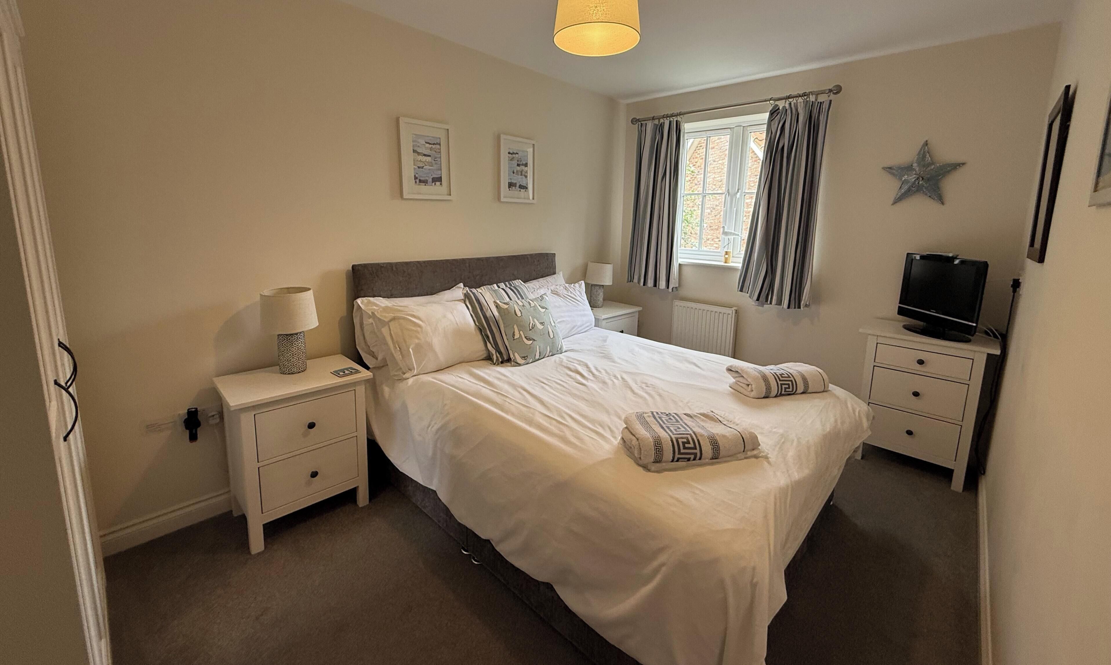 A bedroom with a bed, bedside tables, a lamp, a TV, and a window with curtains.