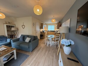 A modern living room with a sofa, dining table, and kitchen in the background.